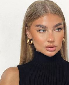 a woman with blonde hair wearing gold hoop earrings and a black turtle neck sweater top