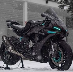 a black motorcycle parked in the snow next to a building and tree with snow falling on it