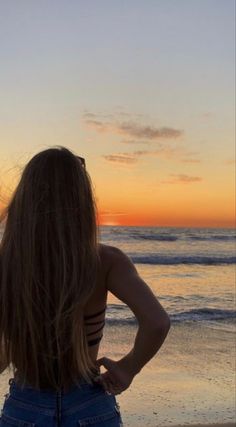 a woman standing on top of a sandy beach next to the ocean at sun set