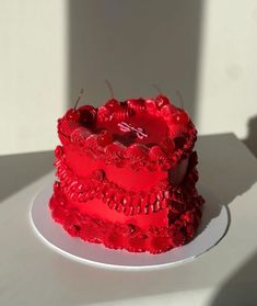 a red cake sitting on top of a white plate covered in frosting next to a shadow