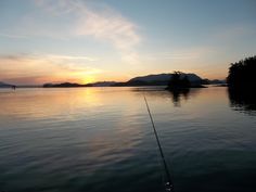 a fishing rod is in the water at sunset with mountains in the backgroud