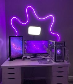 a desk with two computers on it in front of a neon purple wall and white drawers