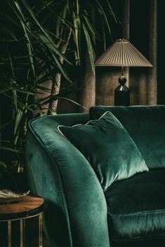 a green couch sitting in front of a lamp next to a table with a vase on it