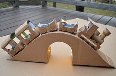 a cardboard train set sitting on top of a wooden table next to a bench and fence