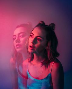 two young women standing in front of a pink and blue background, one looking at the camera