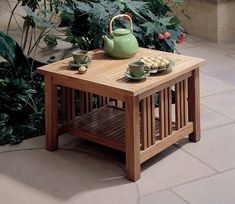 a wooden table with tea cups and plates on it, in front of some potted plants