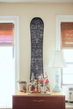 a wooden dresser topped with lots of bottles next to a wall mounted chalkboard sign