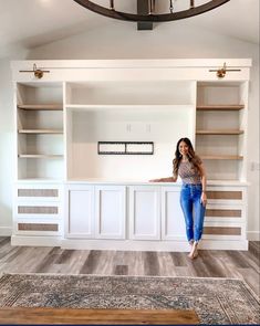 a woman standing in front of a white bookcase with shelving units behind her