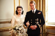 a man and woman standing next to each other in front of a gold framed mirror