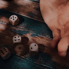 several dices on a wooden table with one hand reaching for the dice to be picked up