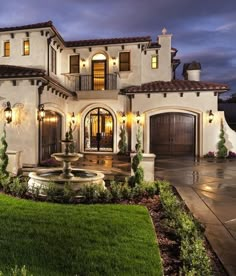 a large house with a fountain in the front yard and landscaping around it at night