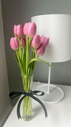 a vase filled with pink tulips on top of a white table next to a lamp