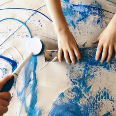 two children are painting with blue and white paint on the paper that they have made