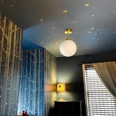 a bedroom decorated in blue and white with trees on the wall, stars painted on the ceiling