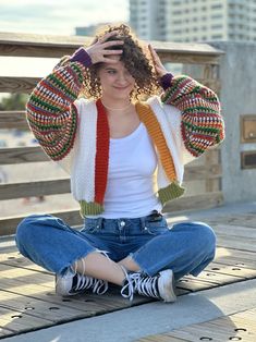 a woman sitting on the ground with her hands in her hair and wearing a colorful cardigan