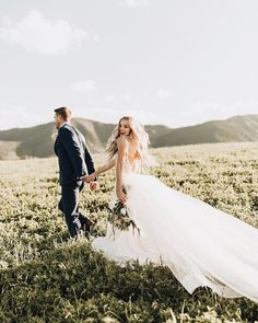 a bride and groom holding hands in a field