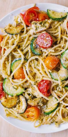 a white plate topped with pasta and veggies on top of a wooden table