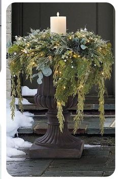 a candle is lit on top of a planter with greenery and pine cones