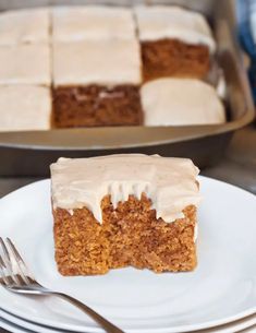 a piece of carrot cake with frosting on a plate next to a knife and fork