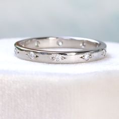 a white gold wedding band with five diamonds on it, sitting on top of a cloth