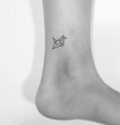 a small origami bird tattoo on the ankle is shown in black and white