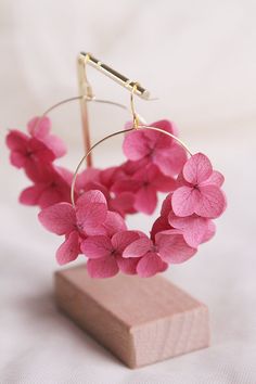 a pair of pink flower hoop earrings sitting on top of a wooden block in front of a white background