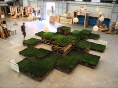 a man standing in front of stacks of green grass covered pallets on the floor