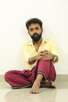 a man sitting on the floor with his hands folded in front of him, wearing a yellow shirt and red pants