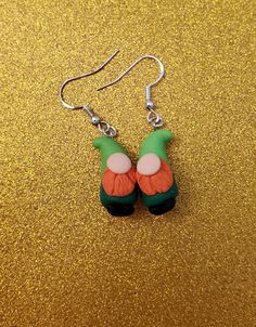 the earrings are green and orange with pink flowers on them, sitting on a gold background