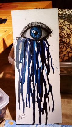 an eye with blue eyes is painted on a piece of white paper and has dripping paint all over it