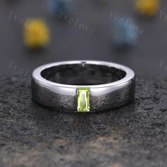 a white gold ring with a green tourmaline stone set in the center, on a granite surface