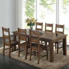 a dining room table and chairs in front of a window with flowers on the rug