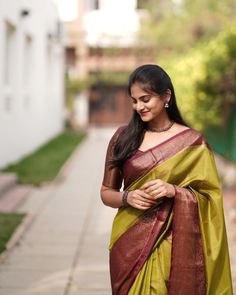 a woman in a green and brown sari walking down the street with her hand on her hip