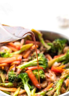 someone is pouring sauce on the stir fry with broccoli, carrots and other vegetables