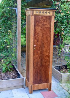 a tall wooden cabinet sitting next to a garden