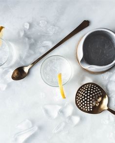 three spoons and two cups on ice with lemon wedges in the bottom one has a strainer