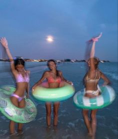 three women in bikinis are standing on the beach with boogie boards and float rings