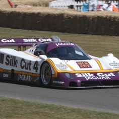 a purple and white race car driving on a track with grass in the foreground