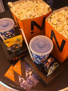 three orange buckets filled with popcorn sitting on top of a table next to other snacks