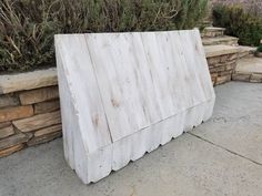 a wooden bench sitting on top of a sidewalk next to a stone wall and shrubbery