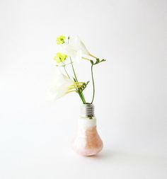 a vase filled with flowers on top of a white table next to a light bulb