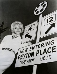 an old black and white photo of a woman standing next to street signs