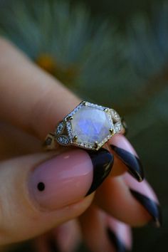 a woman's hand holding a ring with a white stone