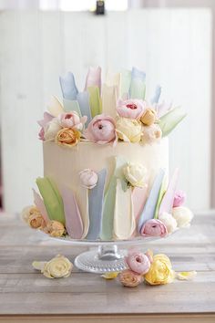 a multi - colored cake with flowers on top sits on a table next to other desserts