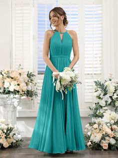 a woman standing in front of flowers wearing a long blue bridesmaid dress with halter neckline