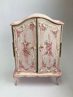 an old fashioned pink and white cabinet with flowers on the front, sitting against a gray background