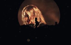 a woman with blonde hair standing in front of a dark background