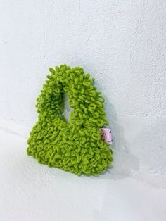 a green knitted object hanging on the wall with a pink ribbon around it's corner