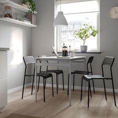 a table with chairs and a laptop on it in front of a window next to a plant