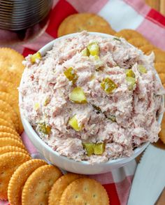 a white bowl filled with tuna salad surrounded by crackers on a red and white checkered tablecloth